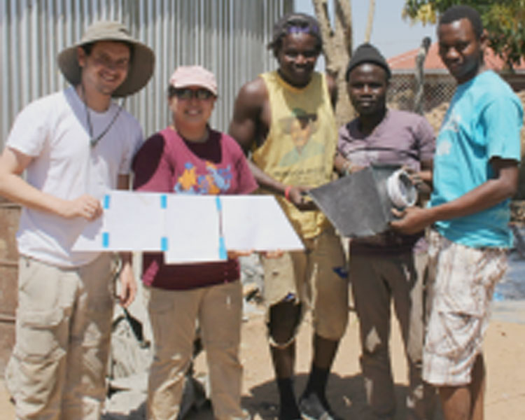 Drew, Joy (EWB), Mambo (AEST), Abudalla (AEST), and Juma (AEST) show off the sketch model and final product of the chute for the charcoal grinder. (Photo: Lauren Bustamante)
